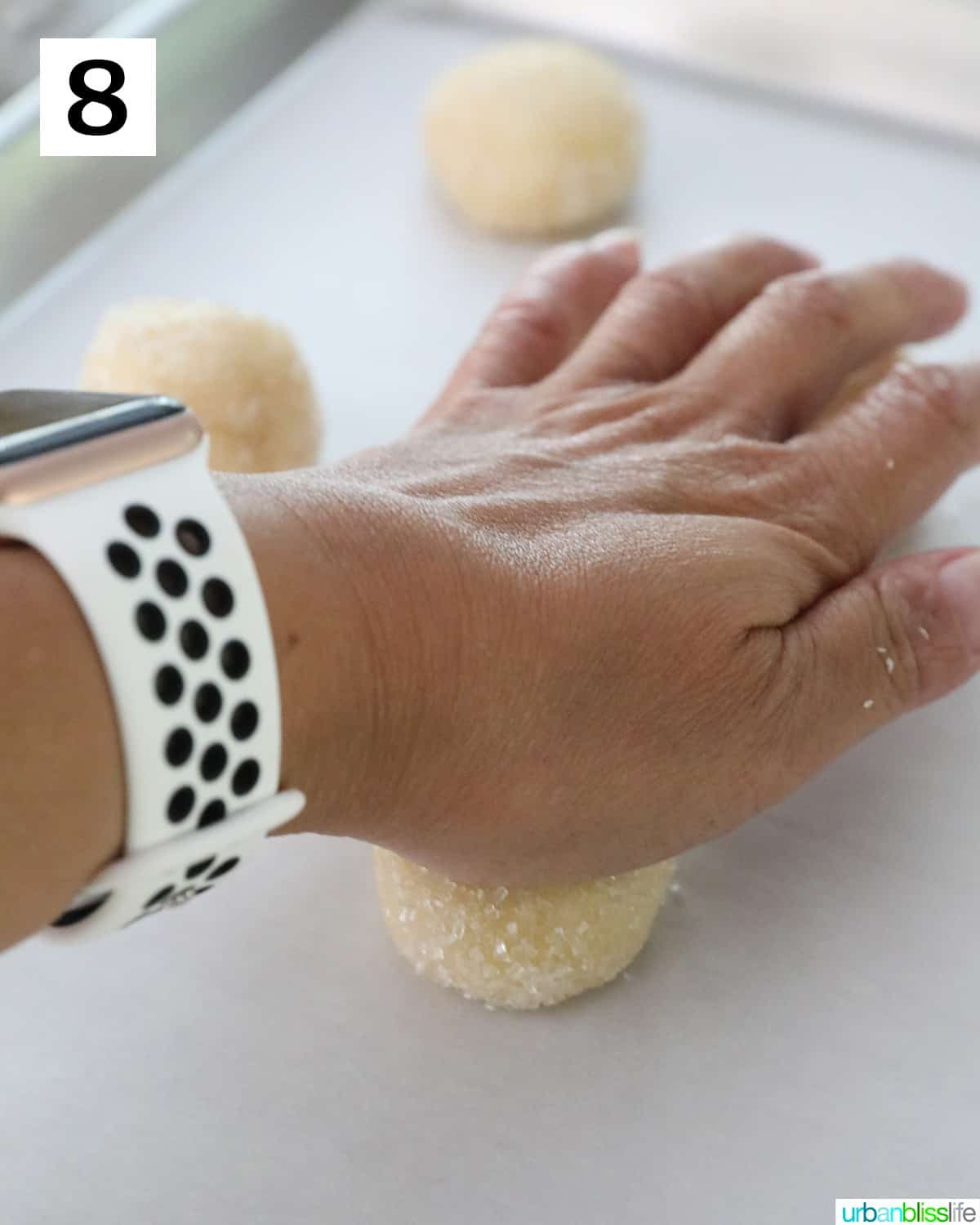 hand pressing a palm down to flatten sugar cookies on a cookie sheet.