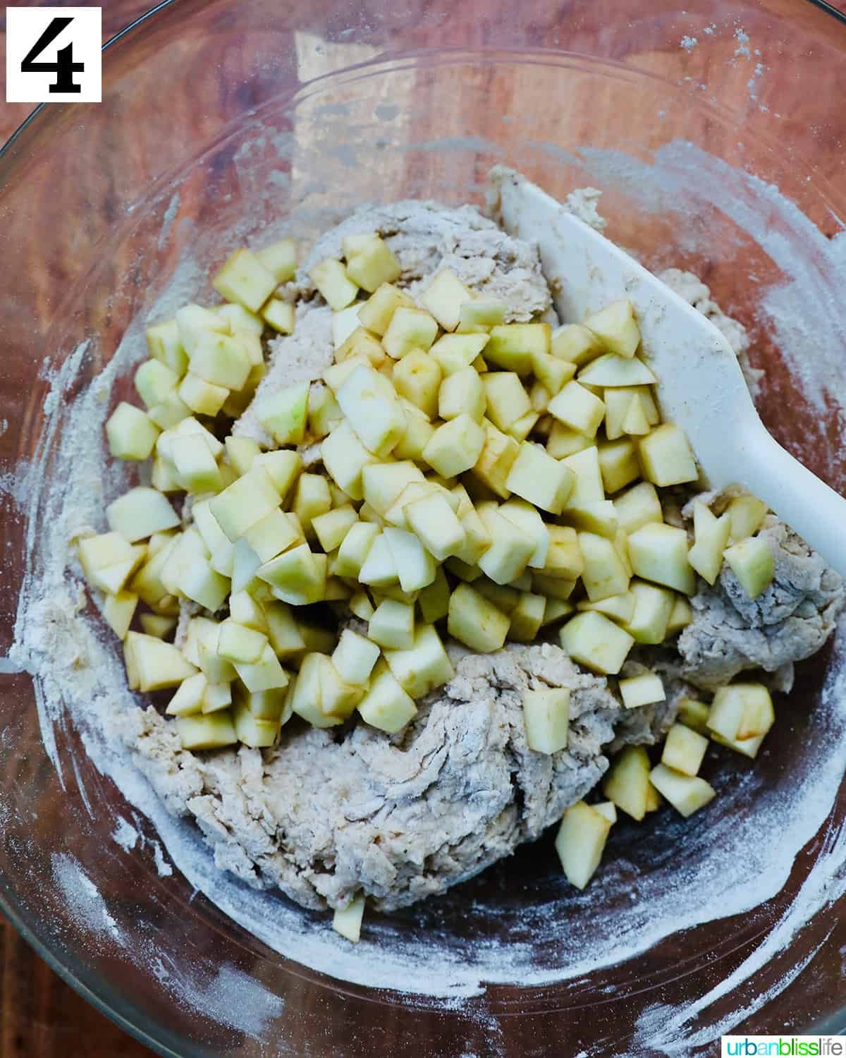diced apples added to apple fritter donut batter in a glass bowl.
