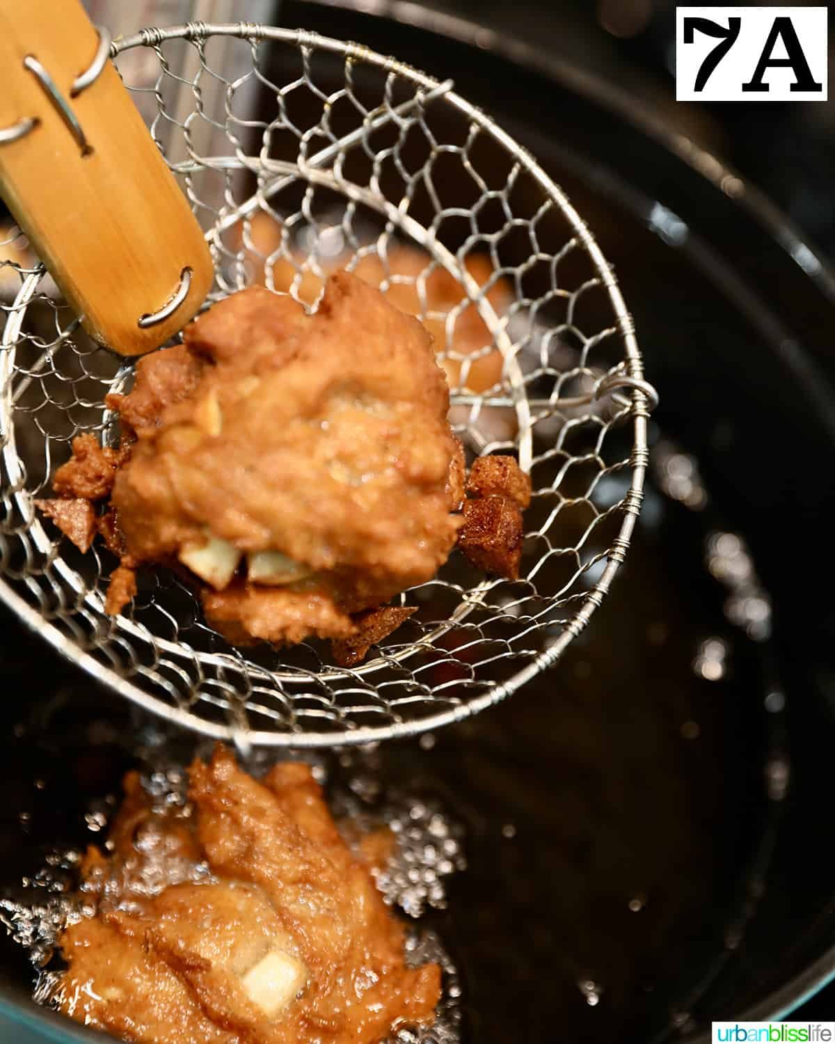 a cooking spider lifting an apple fritter donut out of hot oil.