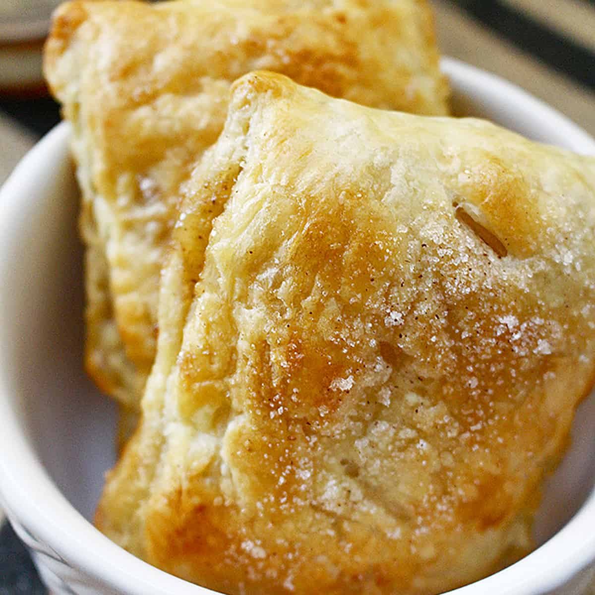 two apple whiskey hand pies in a white bowl.