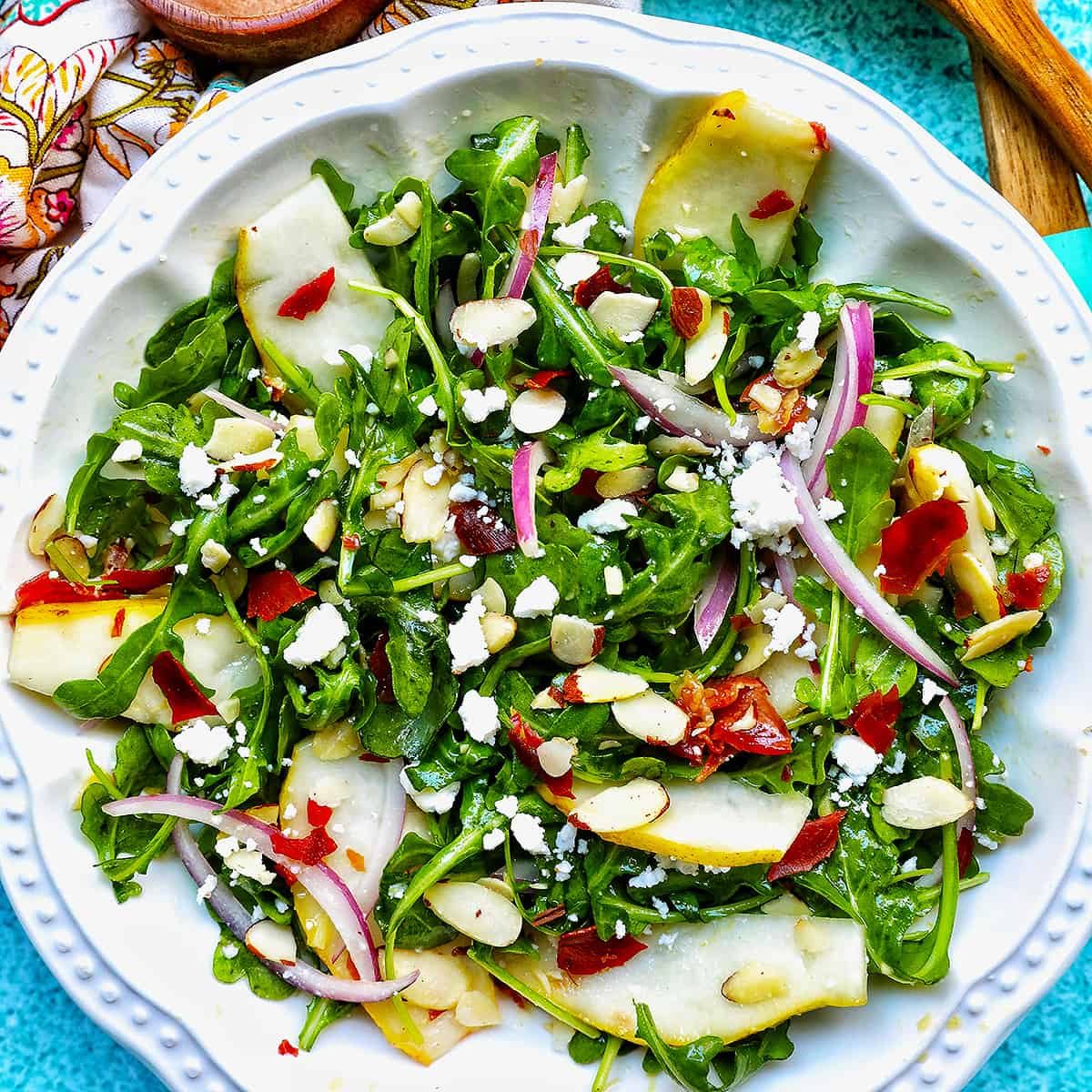 arugula, pears, prosciutto, and red onion salad in a white bowl.