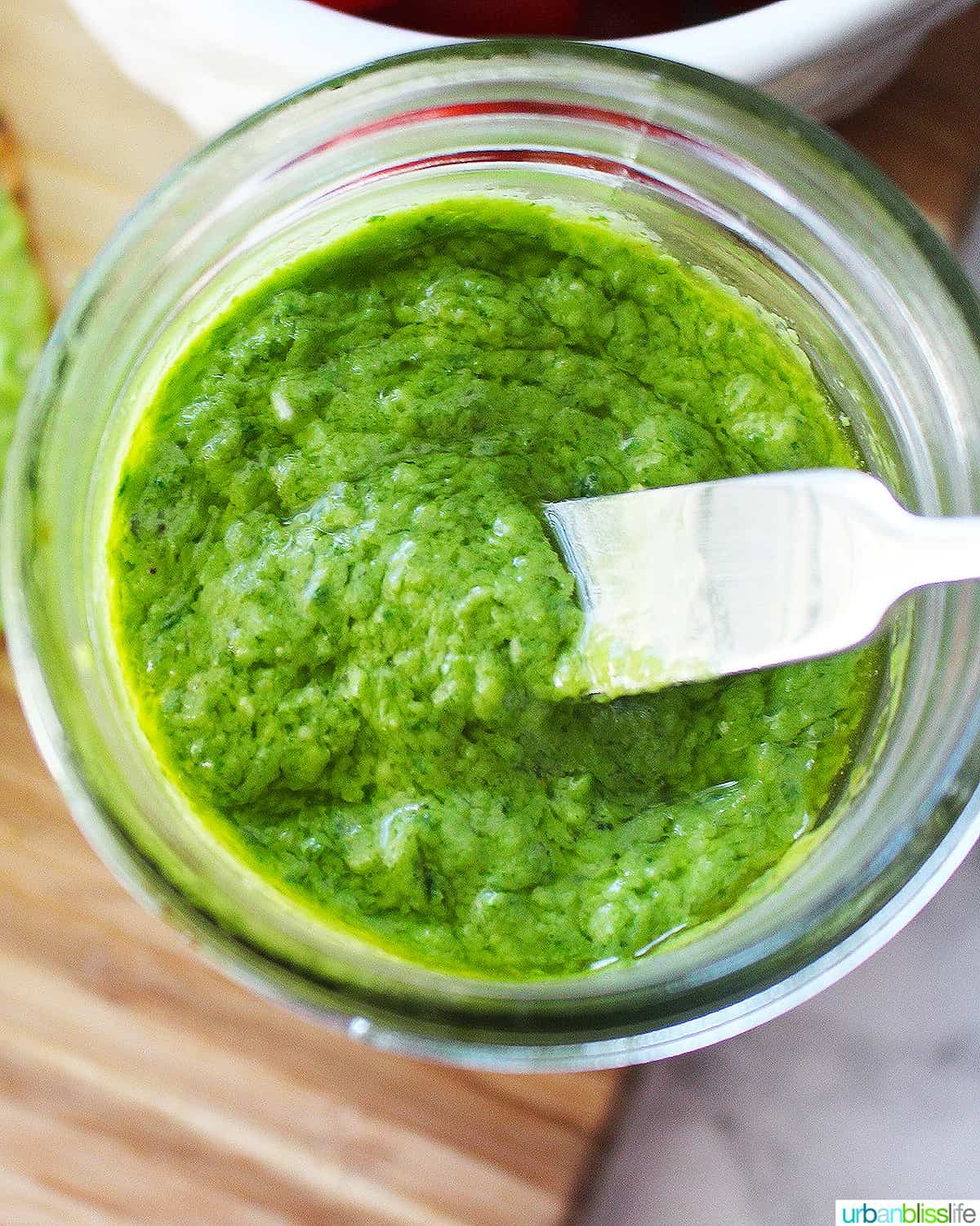 bright green avocado pesto in a mason jar with a small knife placed in the pesto.