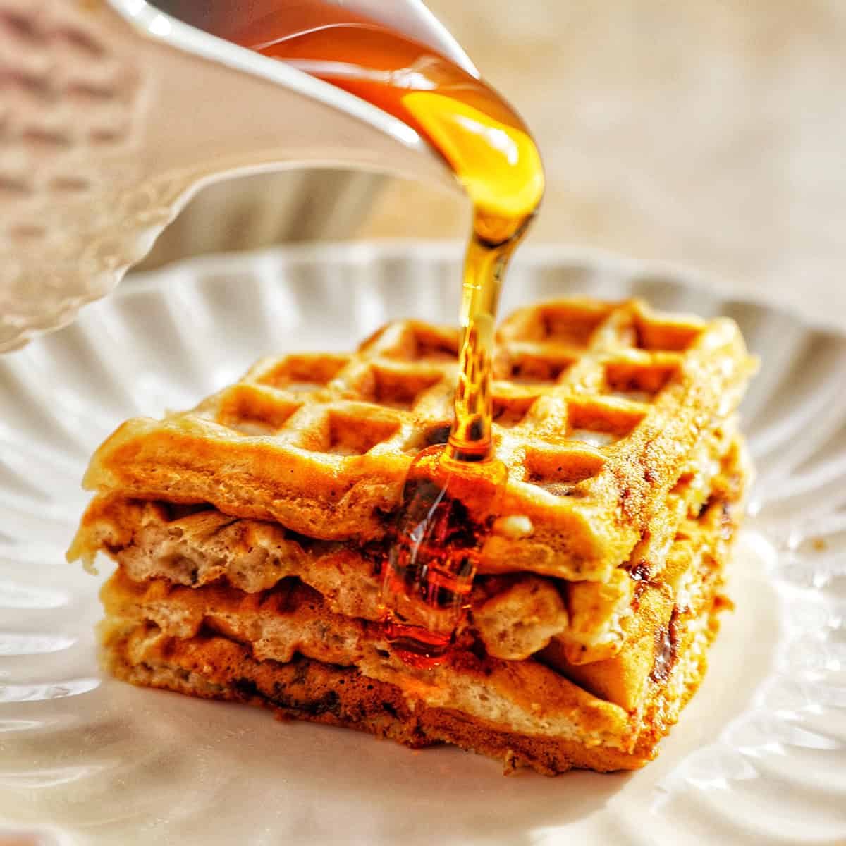maple syrup pouring onto a stack of banana chocolate chip waffles.