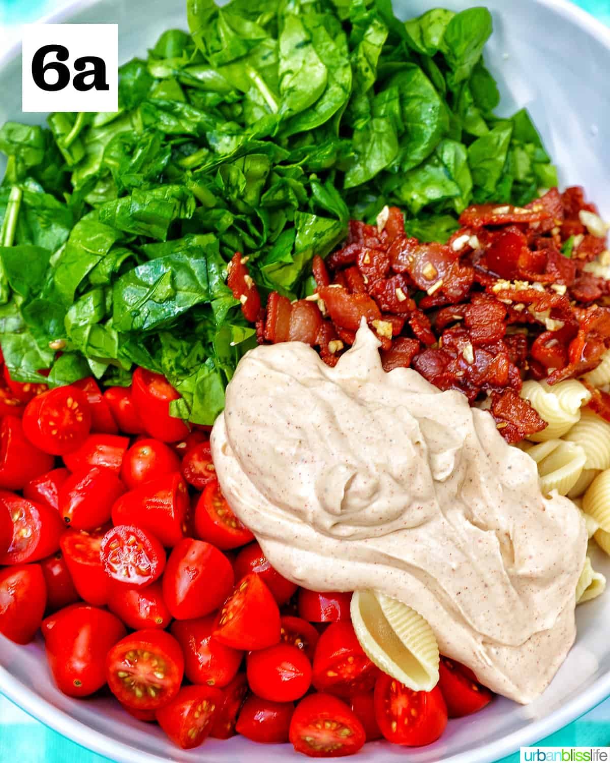 chopped spinach, sliced tomatoes, cooked bacon, pasta shells, and dollop of dressing in a white bowl.