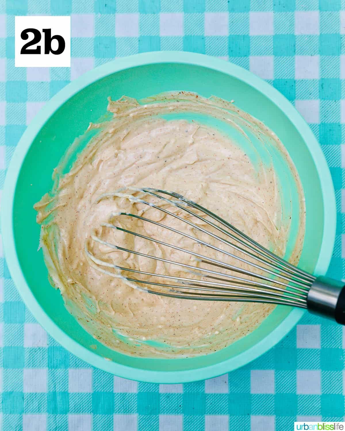 sauce for BLT pasta salad in a green bowl with whisk on an aqua checkered tablecloth.