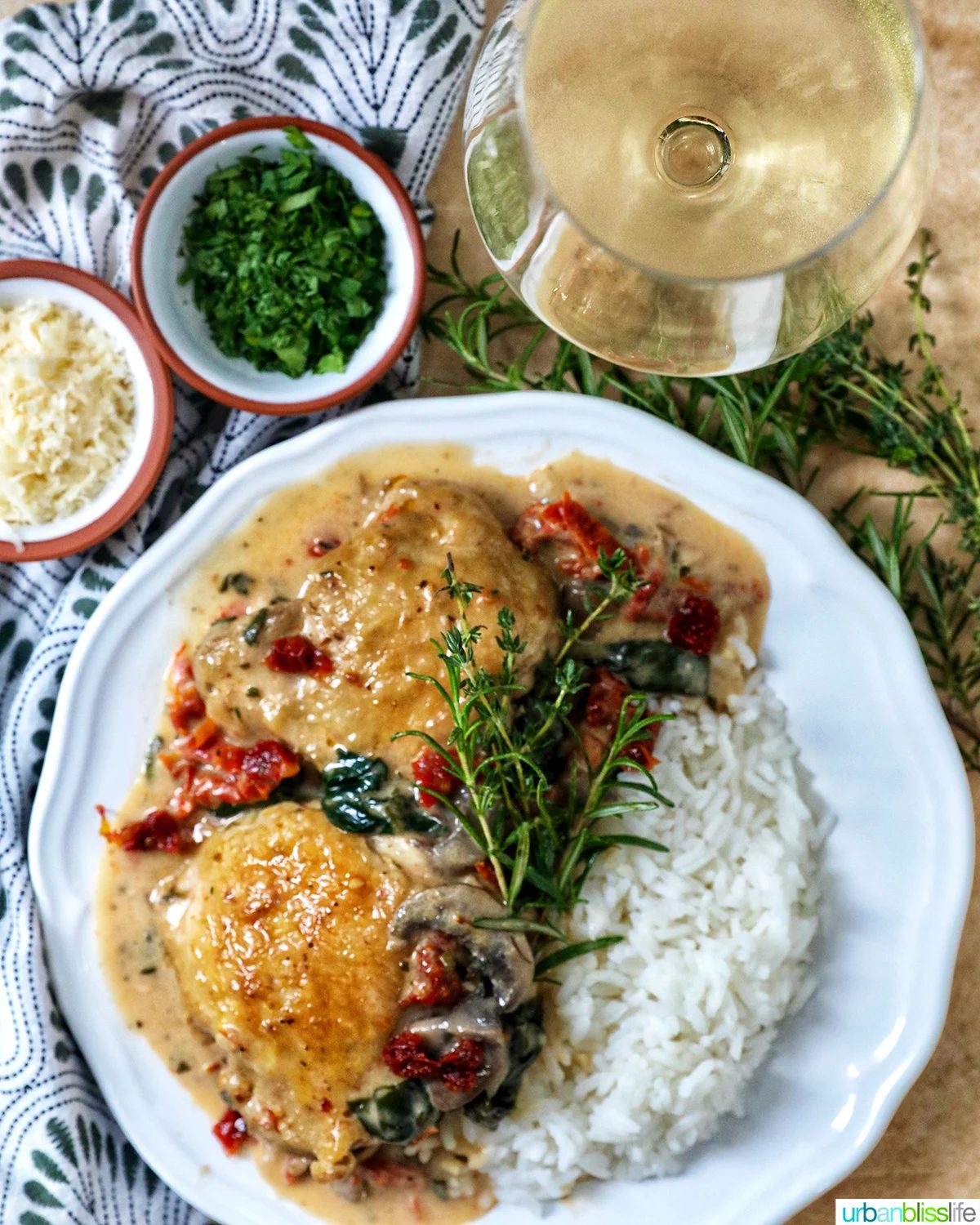 plate of dairy free marry me chicken thighs in a rich mushroom sun-dried tomato sauce with rosemary sprigs and side of rice and glass of white wine.
