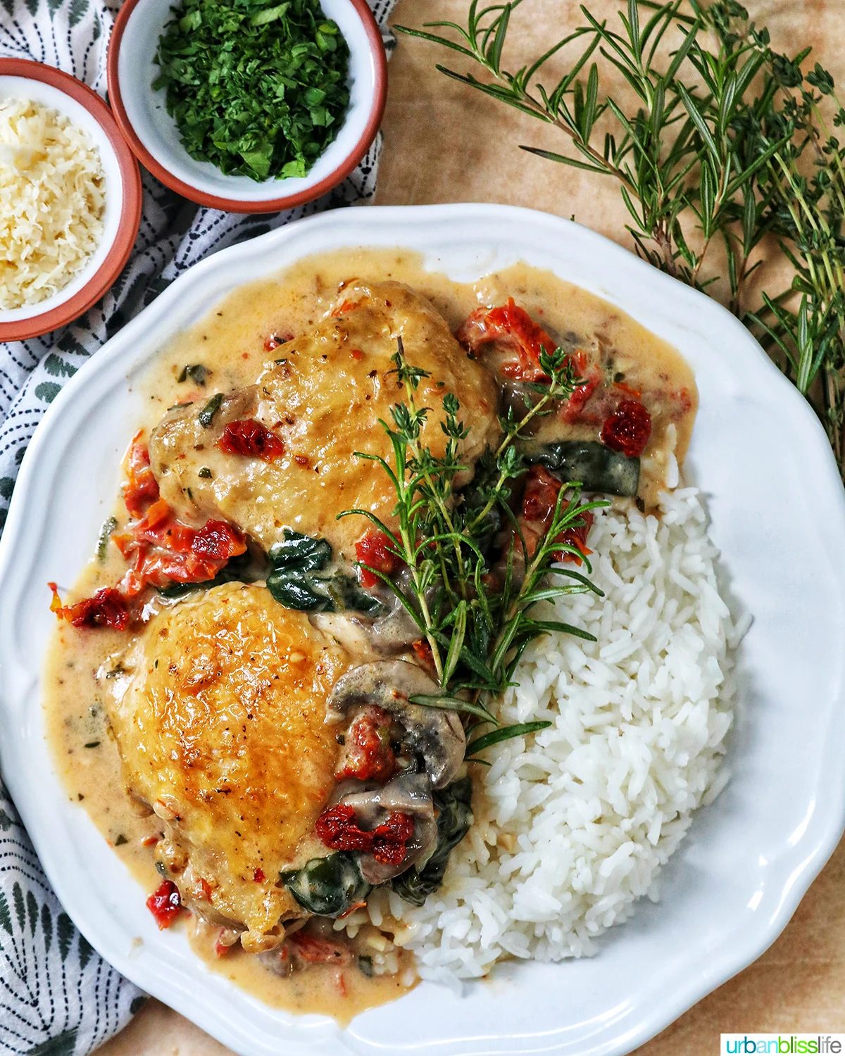 plate of dairy free marry me chicken thighs in a rich mushroom sun-dried tomato sauce with rosemary sprigs and side of rice.