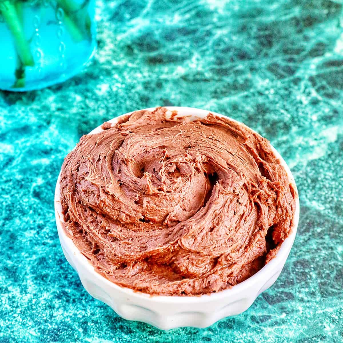 chocolate buttercream frosting in a white bowl on a green marble table.