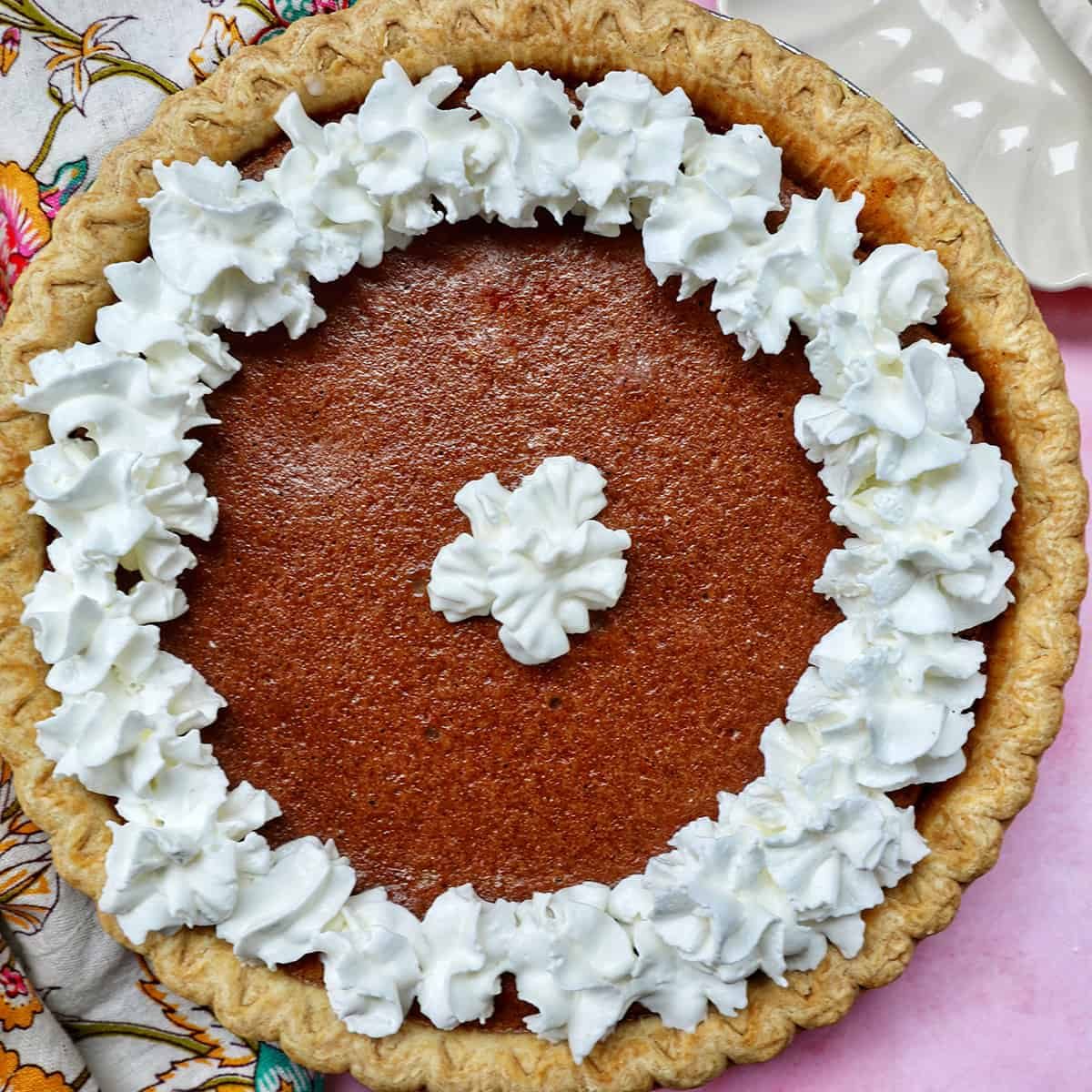 cinnamon pie with whipped cream on a pink background.