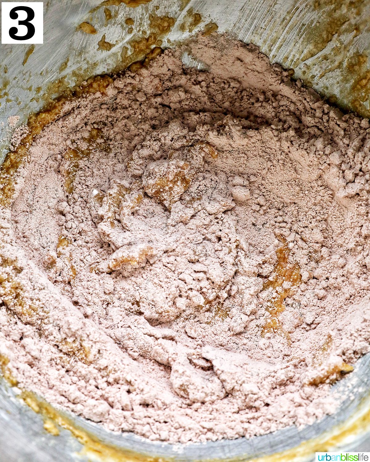 dry and wet ingredients mixing together in a stainless steel bowl of a mixer.