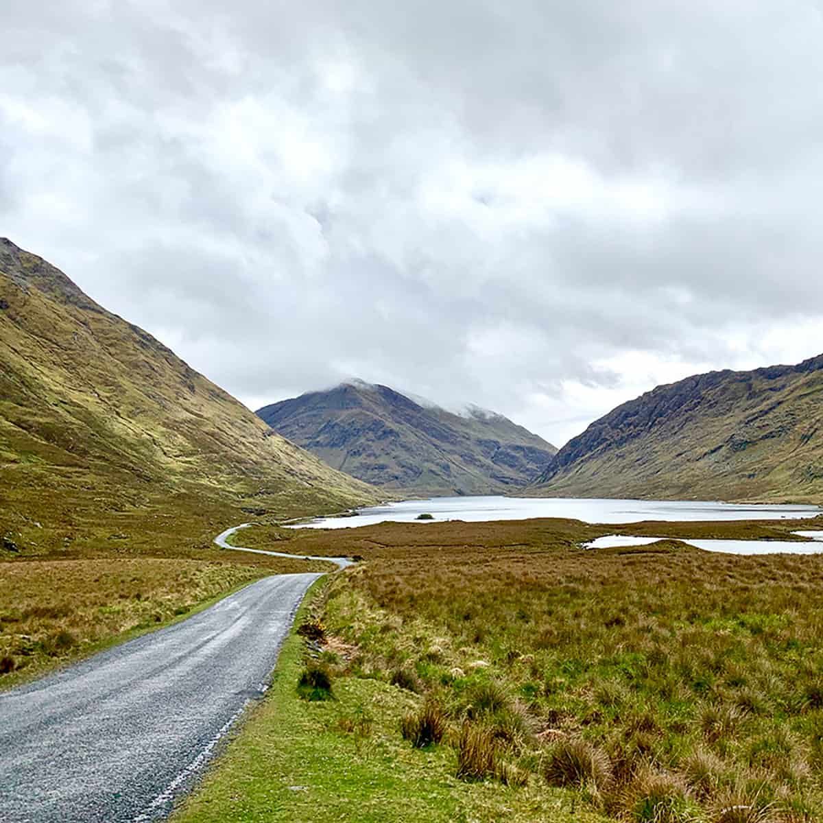 narrow road in ireland with large hills in background