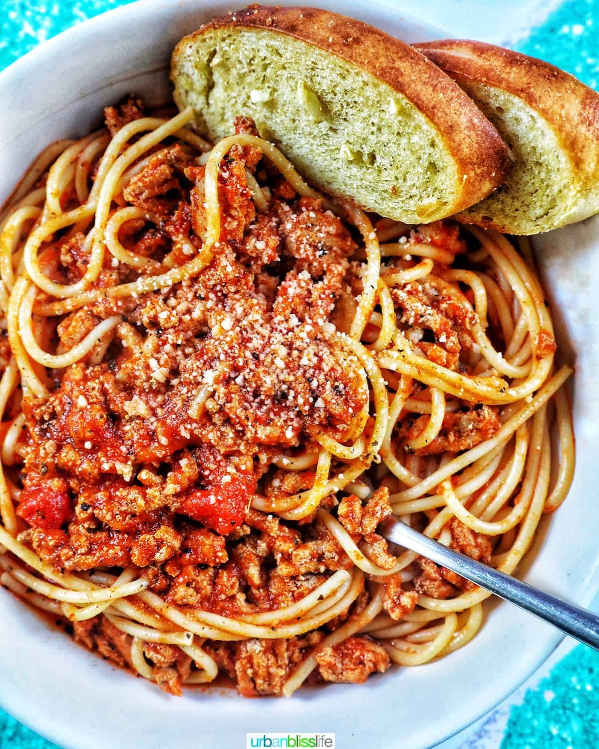 spaghetti and meat sauce with garlic bread in a white bowl.