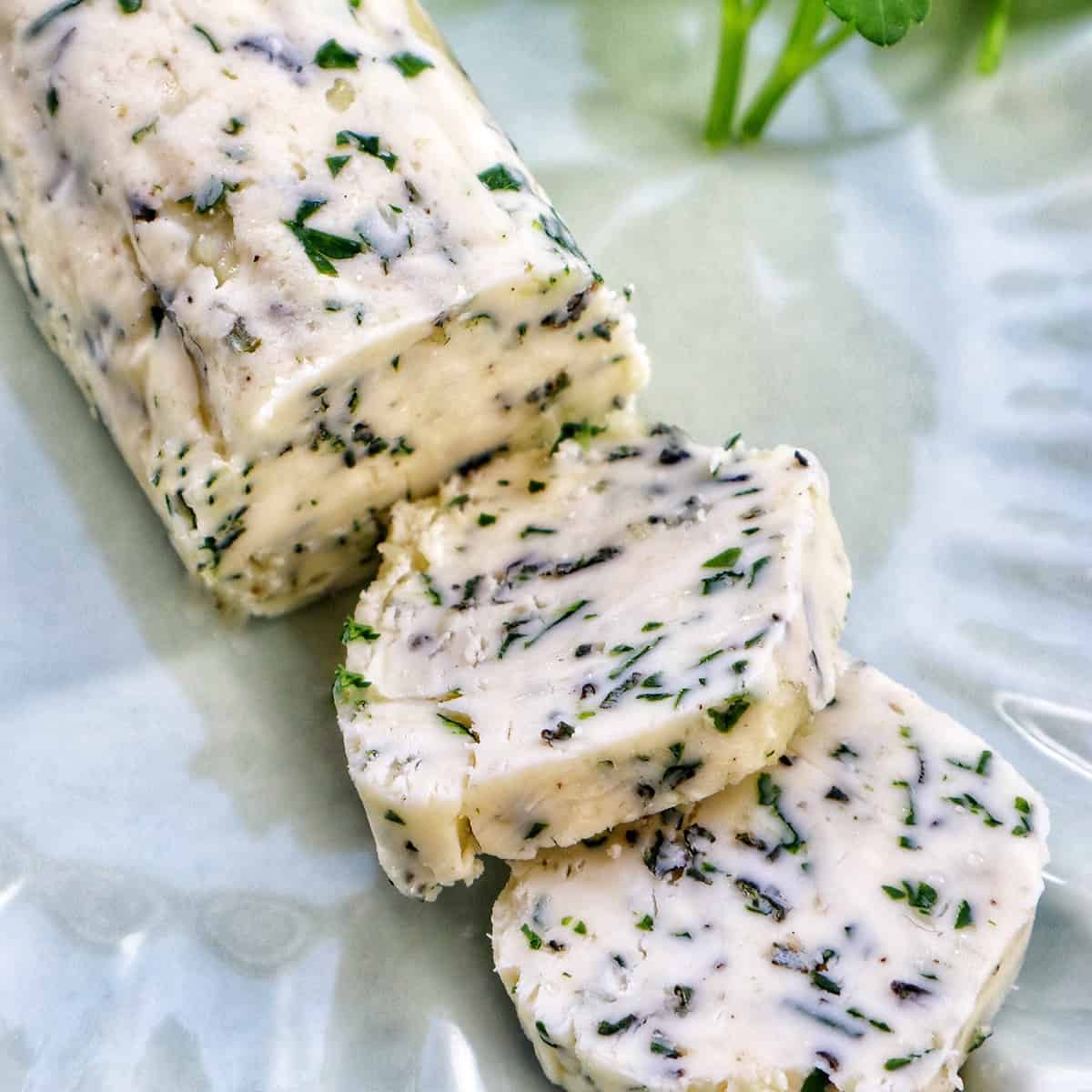 garlic herb compound butter on a green plate with side of herbs.