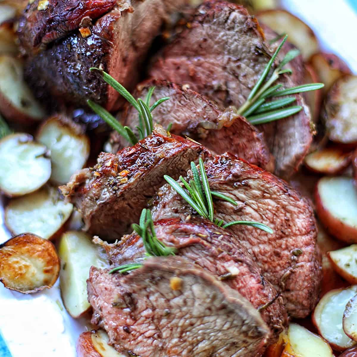 garlic rosemary sirloin tip roast with potatoes on a platter.