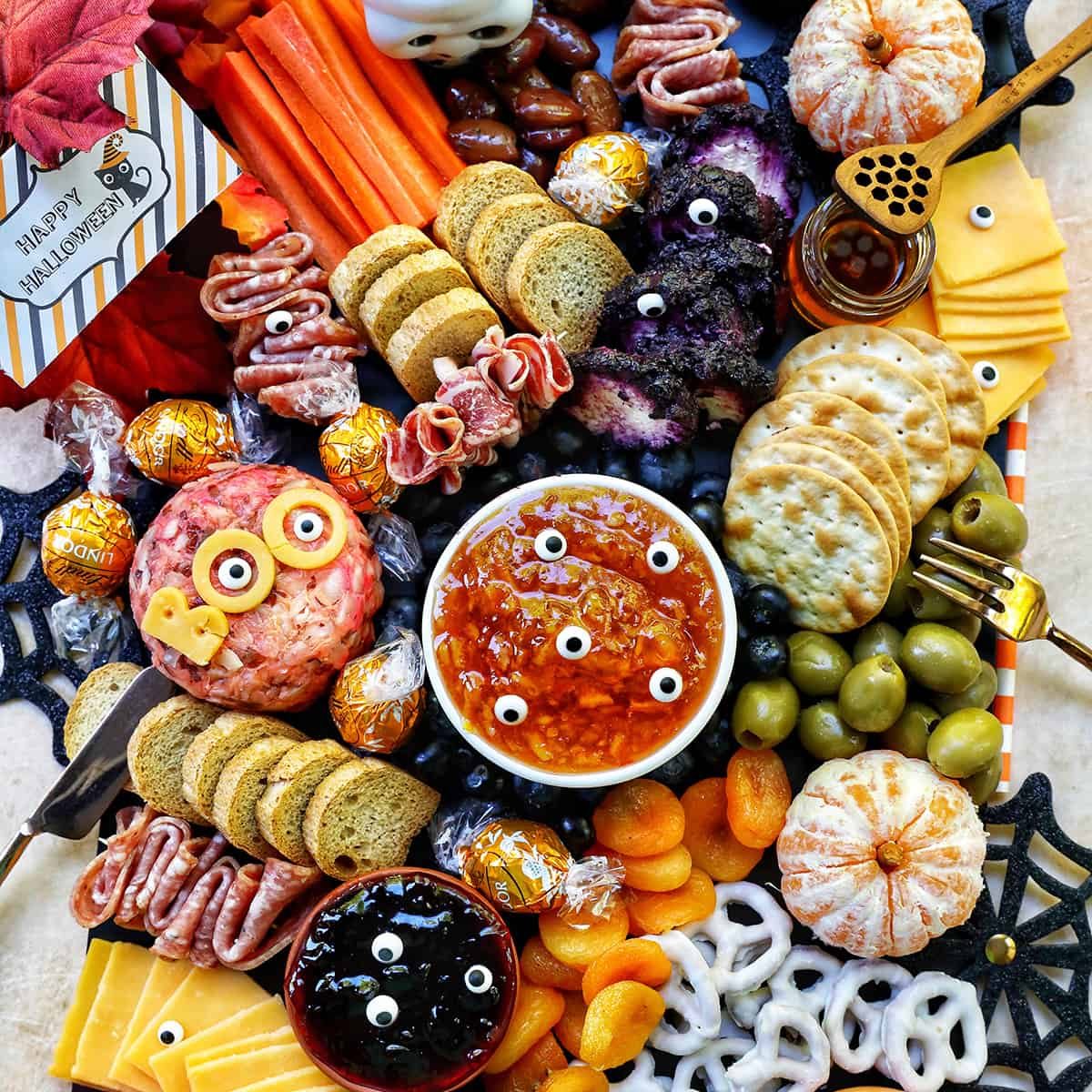 Halloween Charcuterie Board with charcuterie meats, cheeses, crackers, jams, pretzels, fruits, candy eyes, and more orange, purple, and