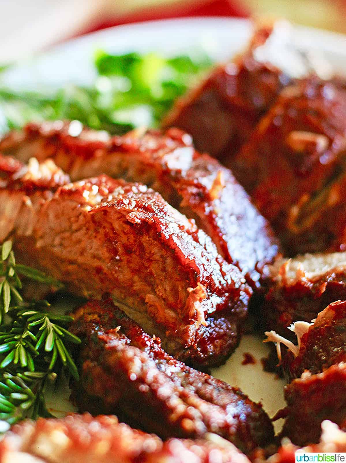 plate full of sliced instant pot pork ribs with rosemary and other herbs.