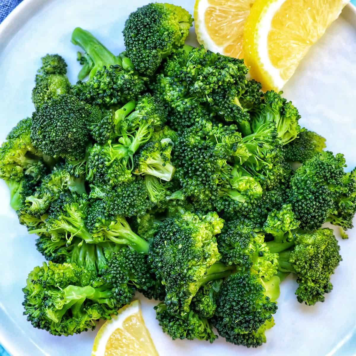 pressure cooked broccoli in a plate with lemon wedges.