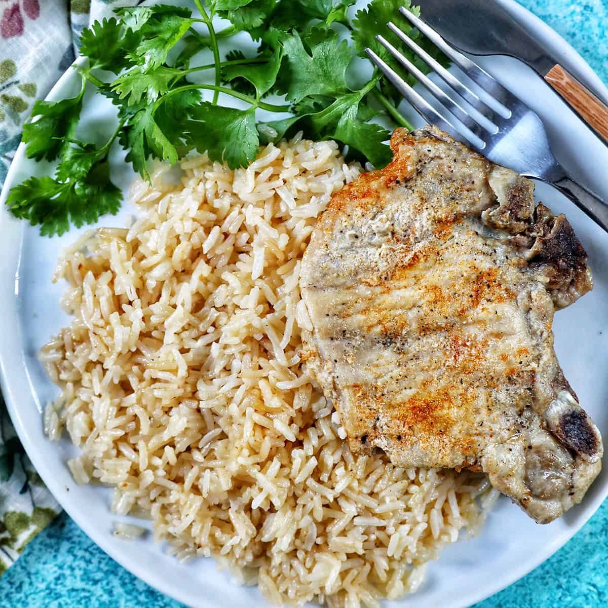 Pressure-cooker Pork Chops and Rice on a white plate with side of greens and fork and knife.