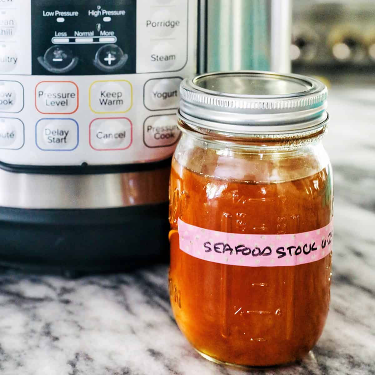 mason jar of seafood stock in front of an Pressure-cooker on marble.