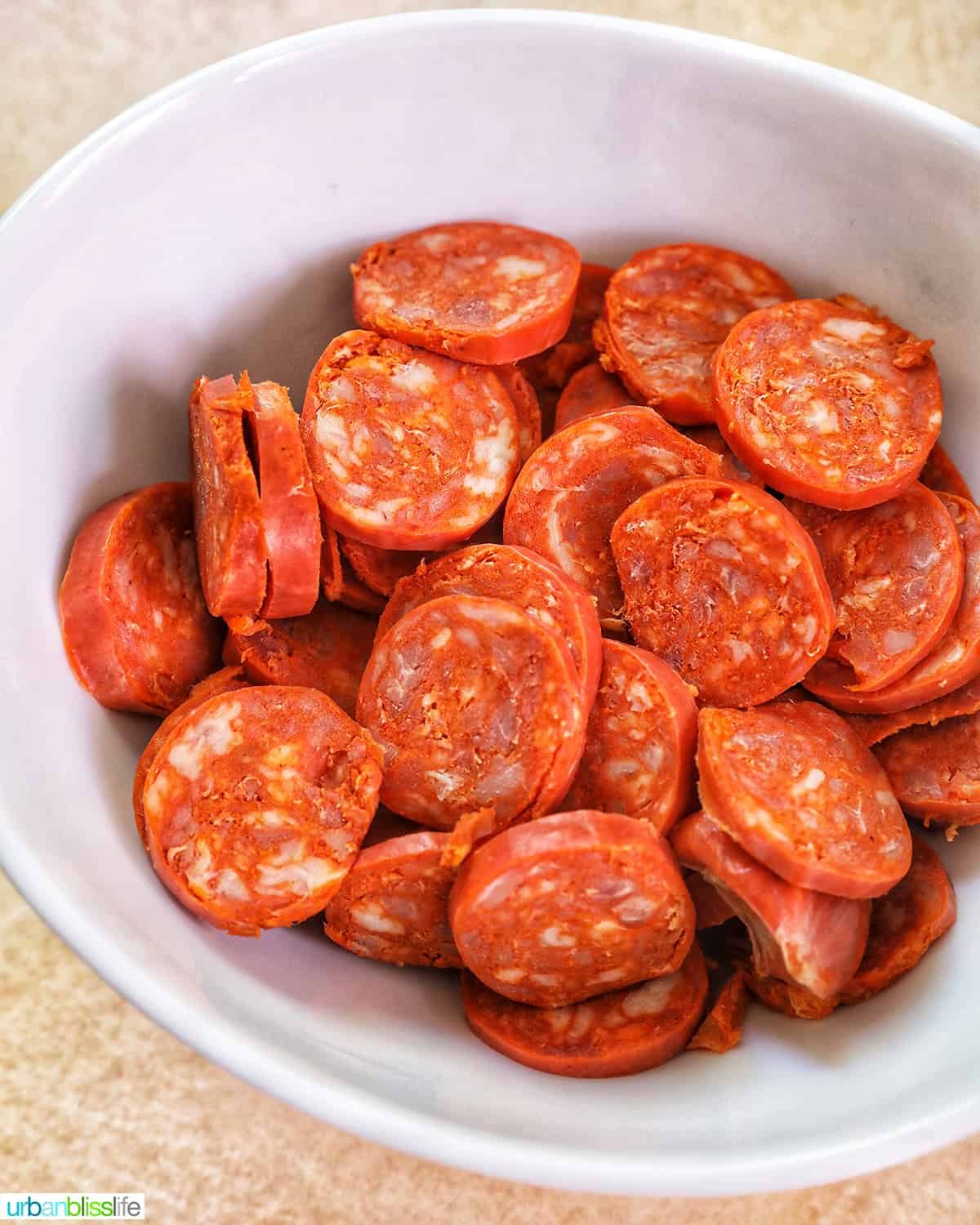 sliced linguica, uncooked, in a white bowl.