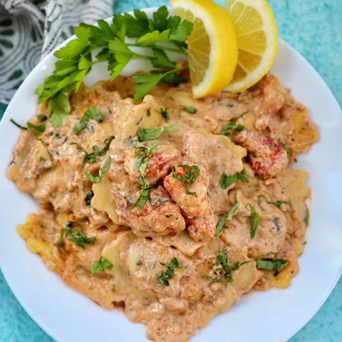 lobster ravioli sauce with lobster meat, lemon wedges, and herbs in a white bowl.