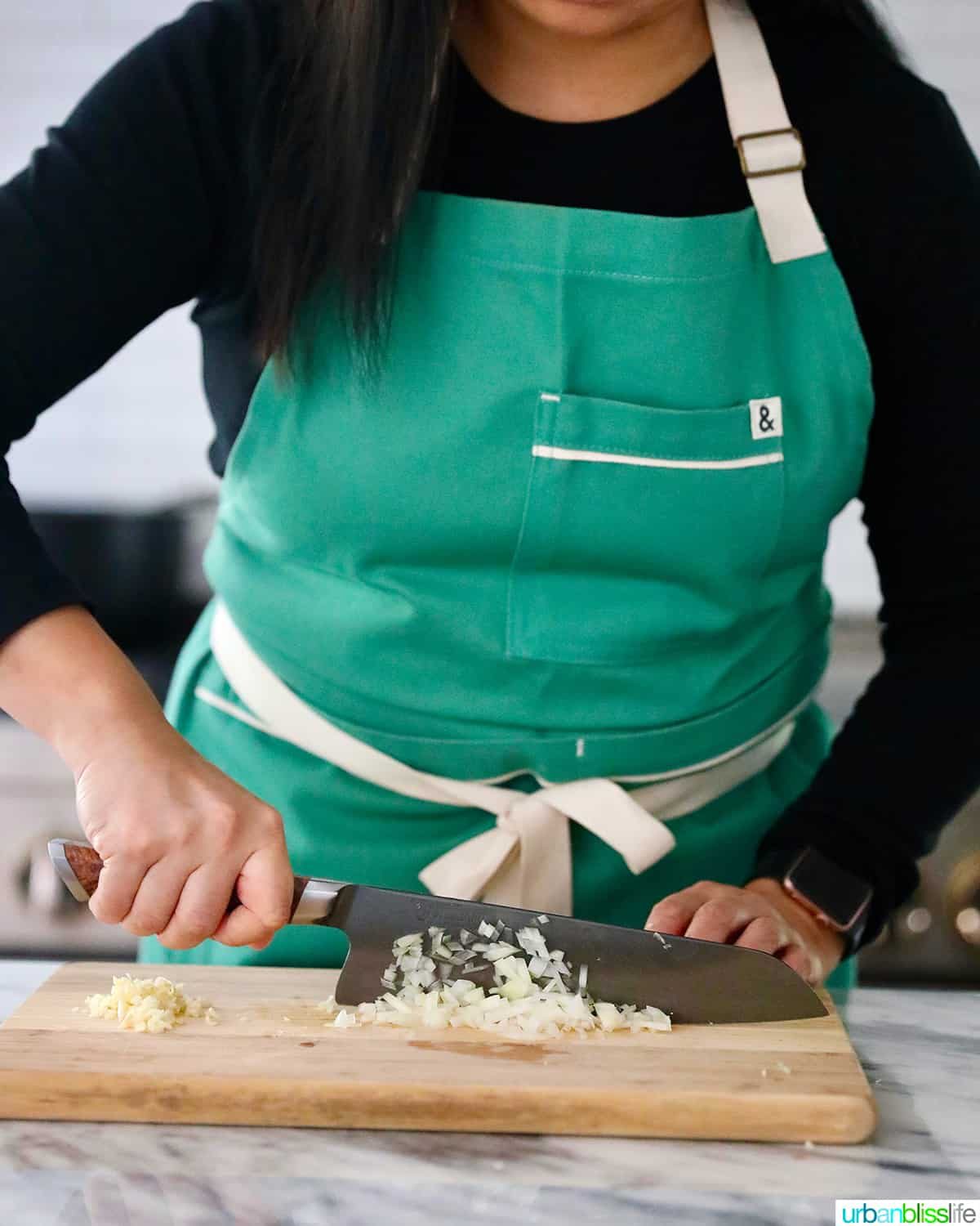 Marlynn wearing Hedley Bennet Apron using a Steelport Knife chopping onions on cutting board