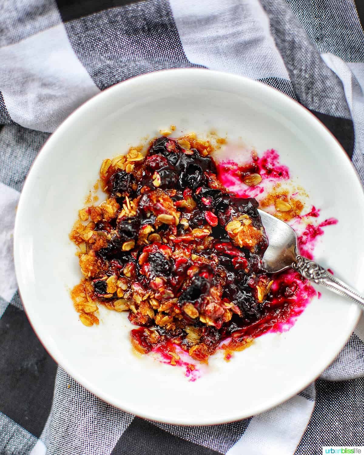 microwave blueberry crisp in a white bowl with checkered backgroud