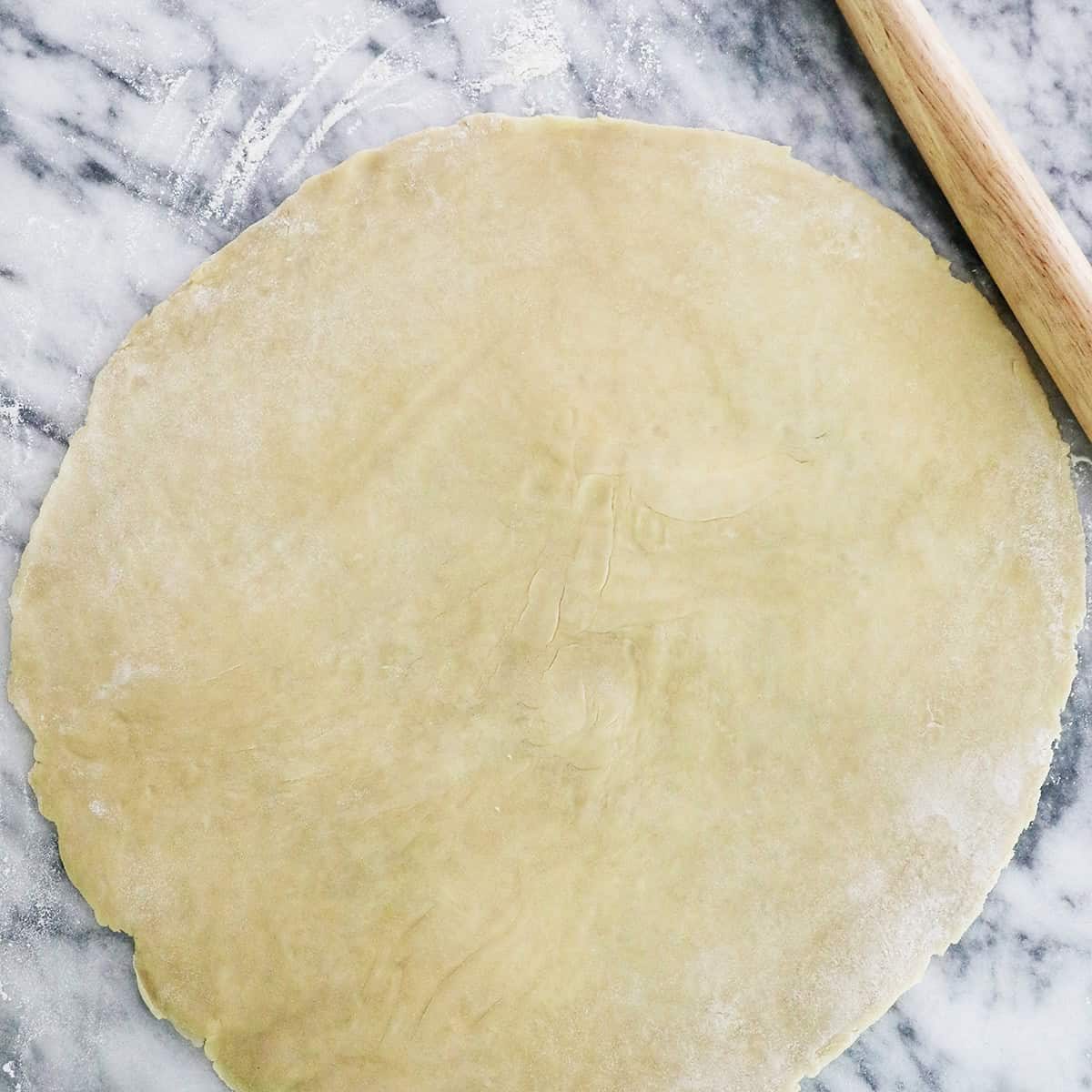 rolled out pie on marble next to a rolling pin.