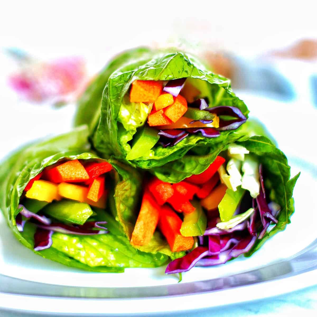 three rainbow salad rolls stacked on a plate.