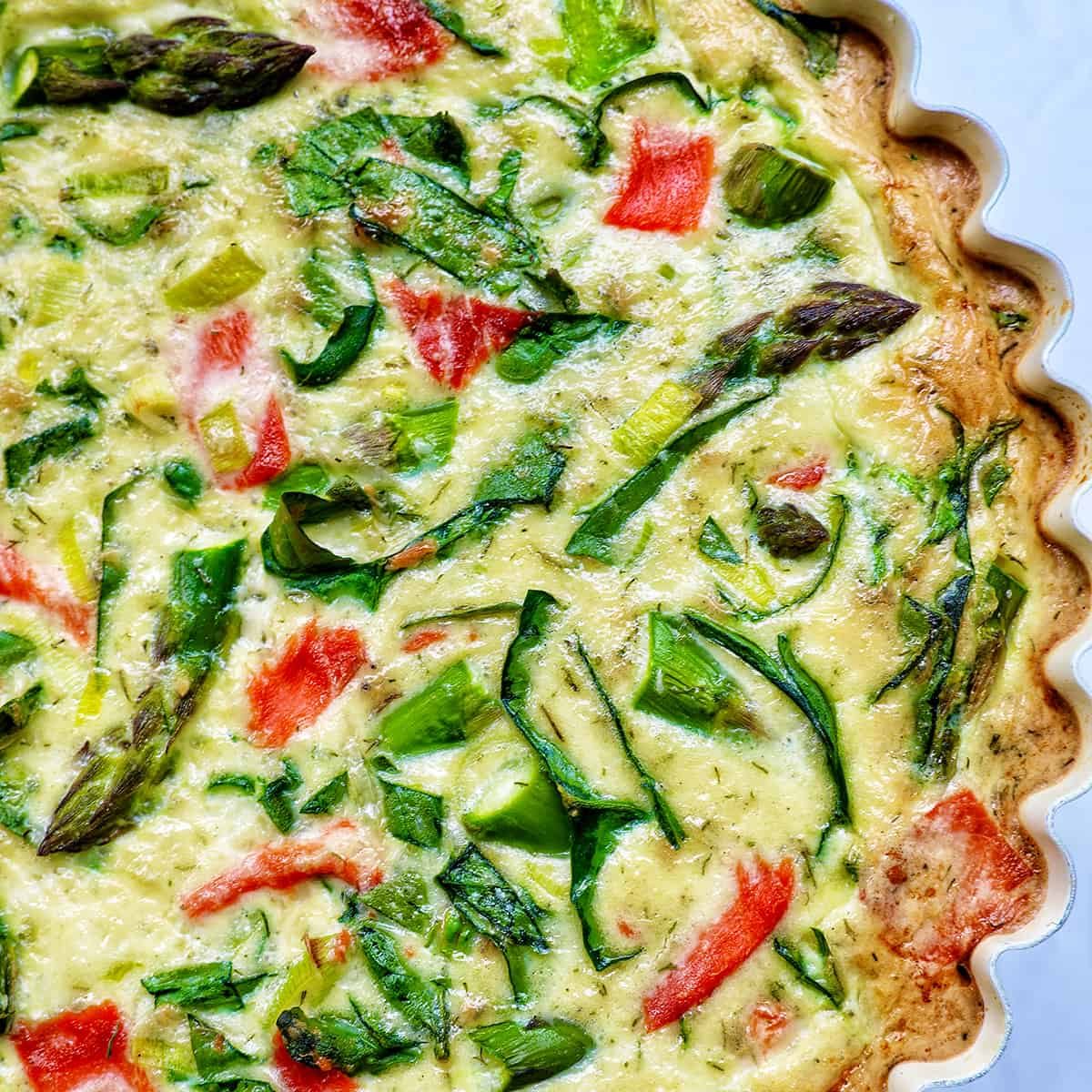 Half of a quiche in a pie pan with salmon, asparagus, and leeks.