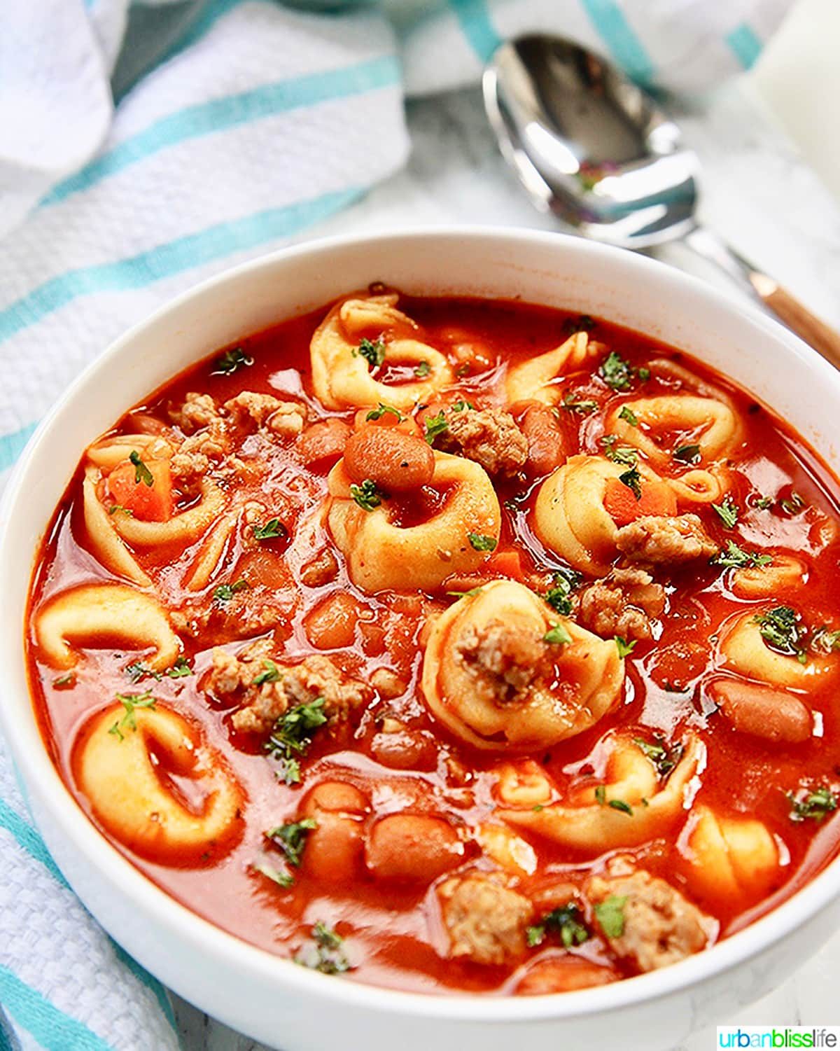 bowl of sausage tortellini soup with spoon on side