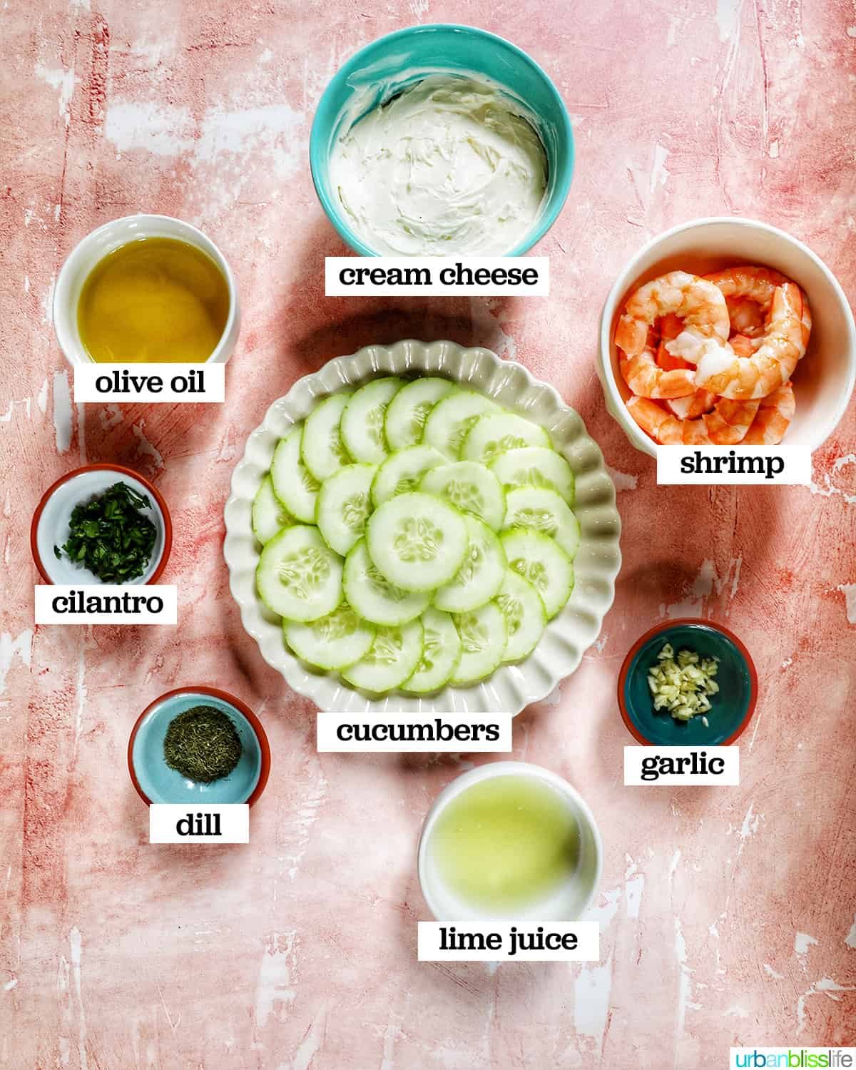 ingredients in bowls and on plates to make cucumber shrimp canapés on a peach background.