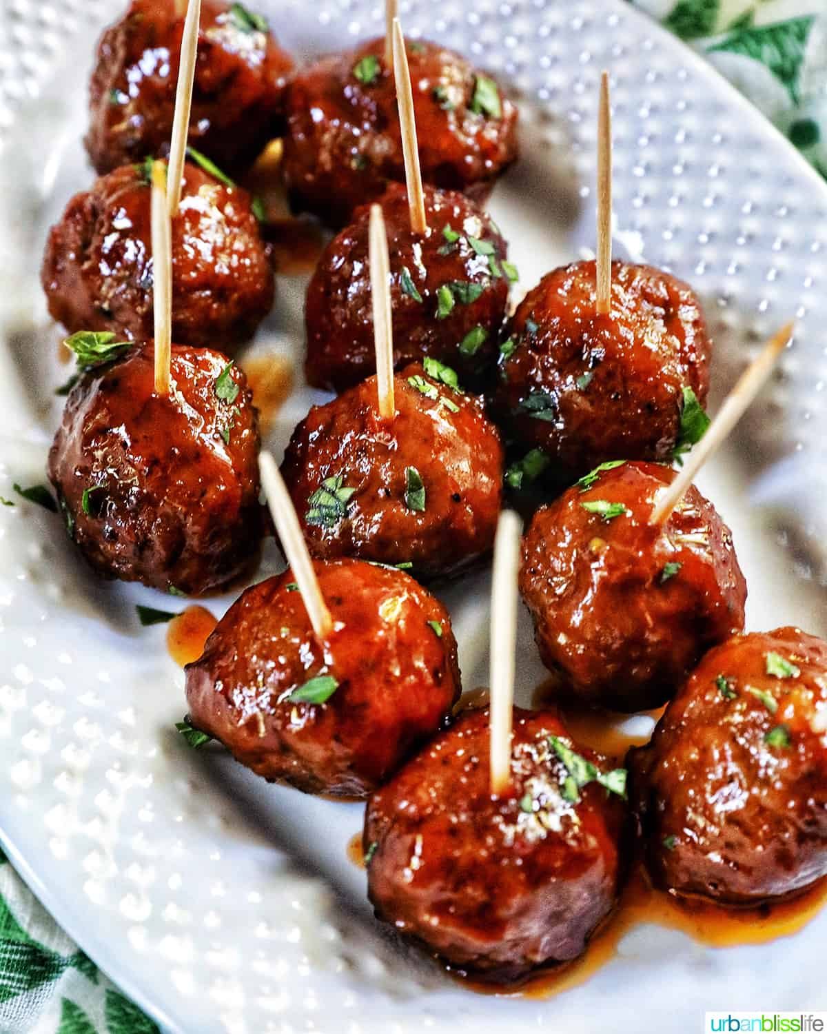 white serving plate with several honey bourbon meatball appetizers with toothpicks in them.