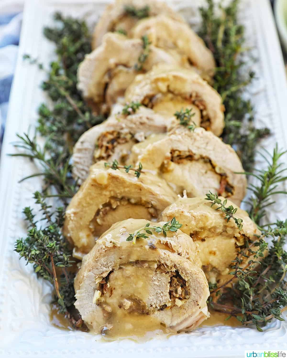 sliced stuffed pork loin on a white plate with a bed of herbs.