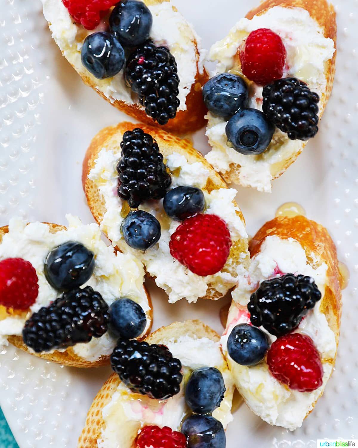 Ricotta crostini with summer berries arranged on a white serving platter.