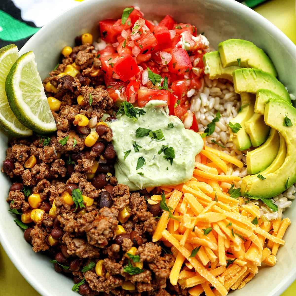 taco bowl with ground beef, beans, cheese, pico de gallo, avocado, rice, avocado cilantro lime crema.
