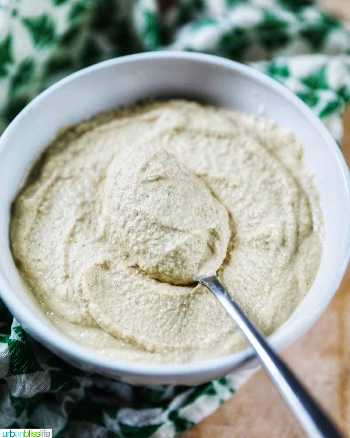 whitwhite bowl of Vegan Cashew Cheese with spoon in bowl, with green and white napkin underneath.