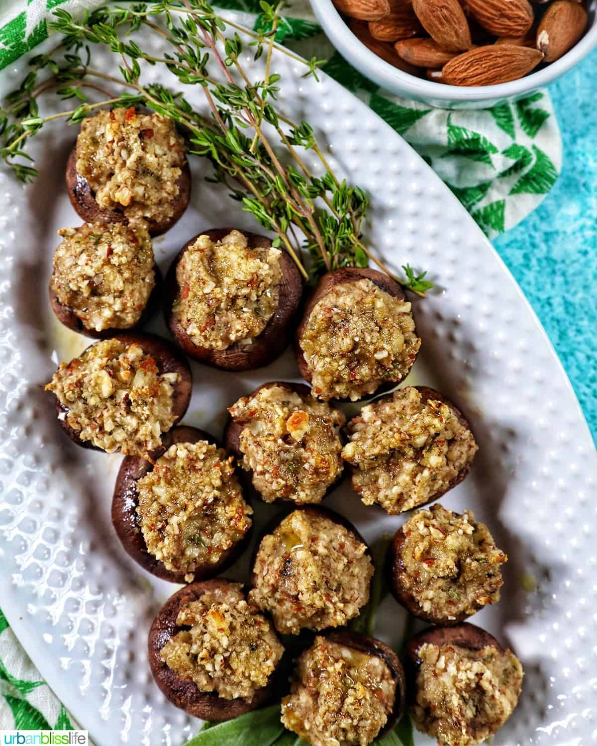 overhead photo of several Vegan Stuffed Mushrooms close together on a white platter with thyme leaves and blue background.