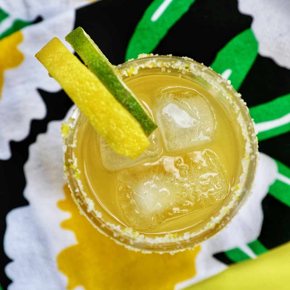 glass of yuzu margarita with slices of lemon and lime on brightly colored napkins.
