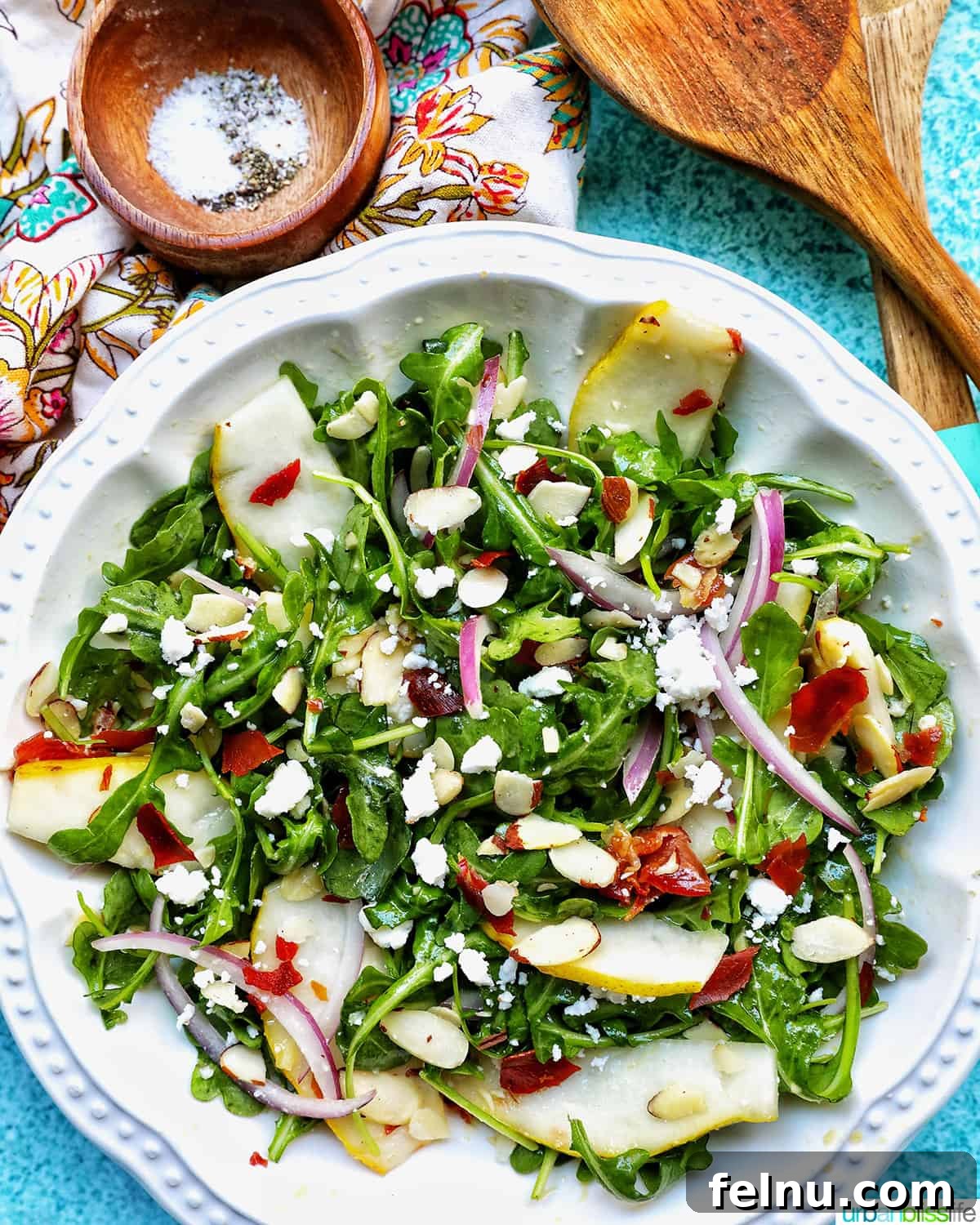 Sweet Pear and Peppery Arugula Salad 2 Large bowl of arugula and pear salad with crispy prosciutto, sliced almonds, and a wooden spoon.
