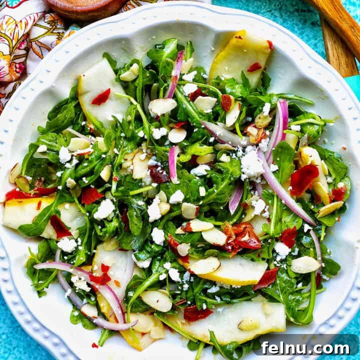 Arugula, pears, prosciutto, and red onion salad in a white bowl.