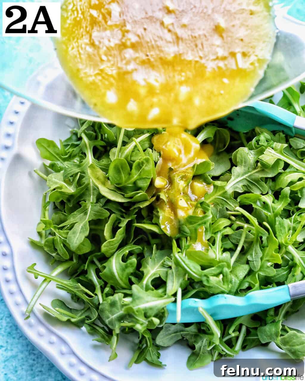 Sweet Pear and Peppery Arugula Salad 8 Pouring lemon mustard dressing over a large bowl of fresh baby arugula leaves.