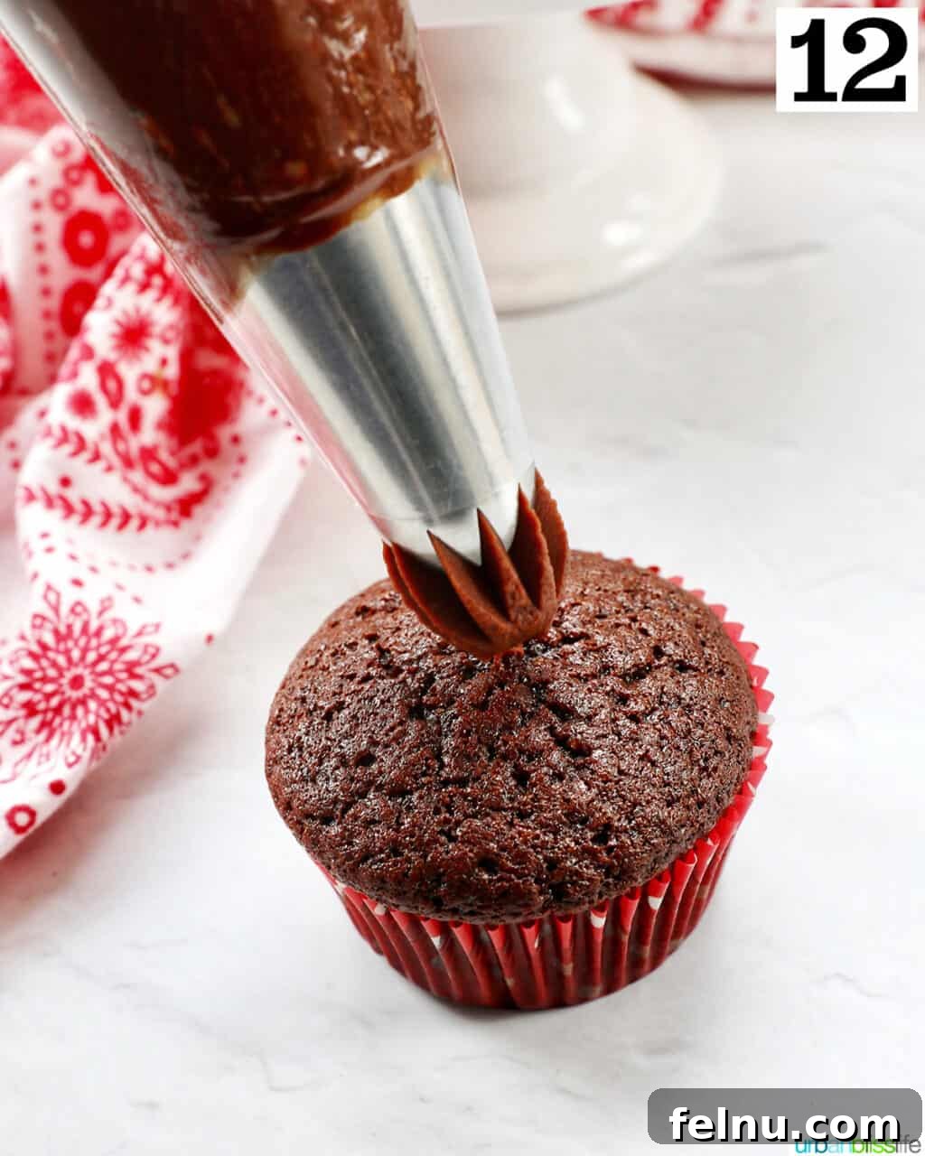 Velvet Chocolate Fudge Cupcakes 18 chocolate ganache frosting piping onto a chocolate fudge cupcake.