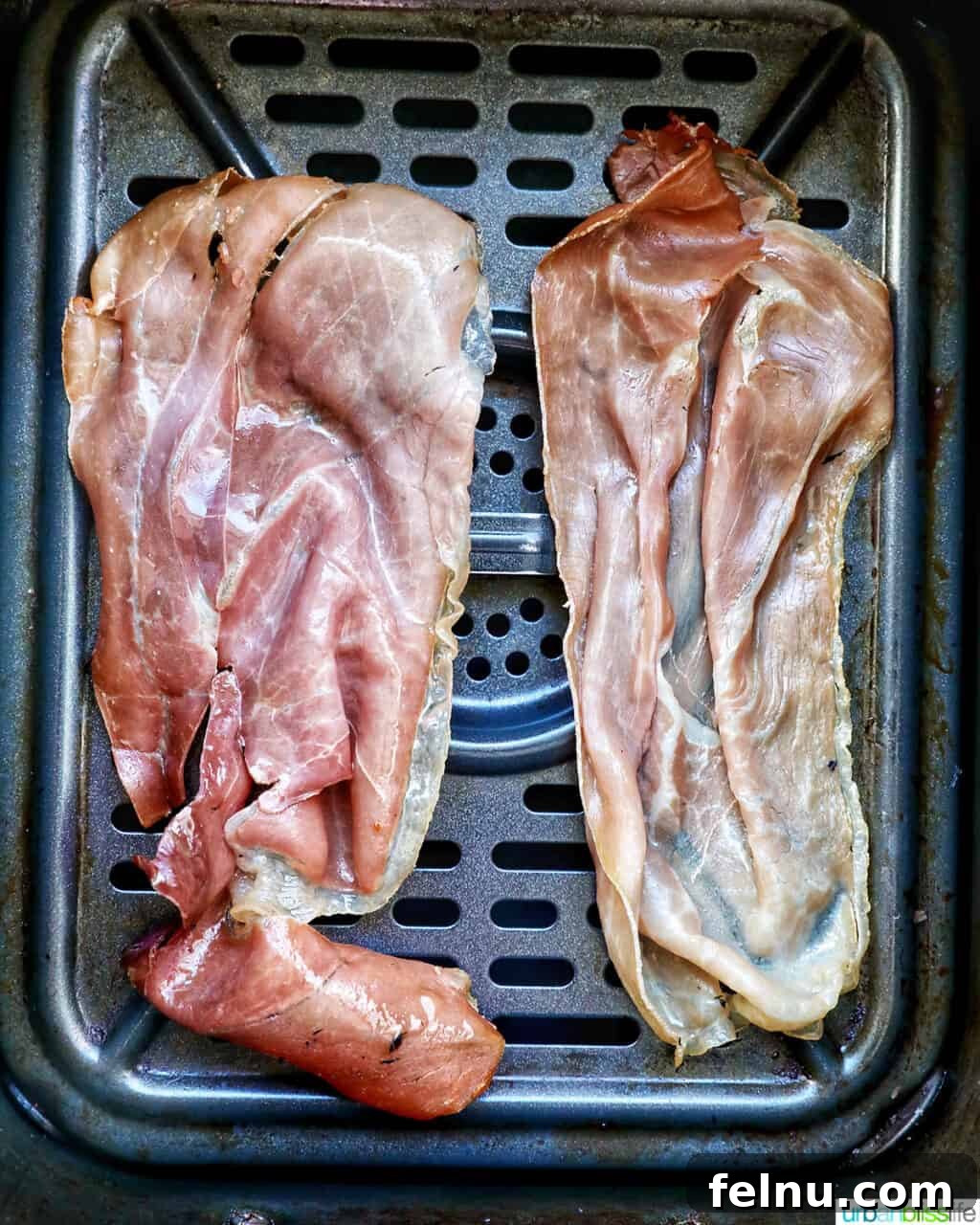 Prosciutto strips arranged in an air fryer basket.