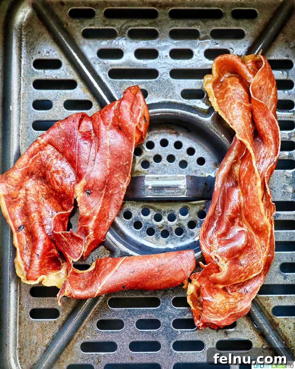 Cooked crispy prosciutto in an air fryer basket.