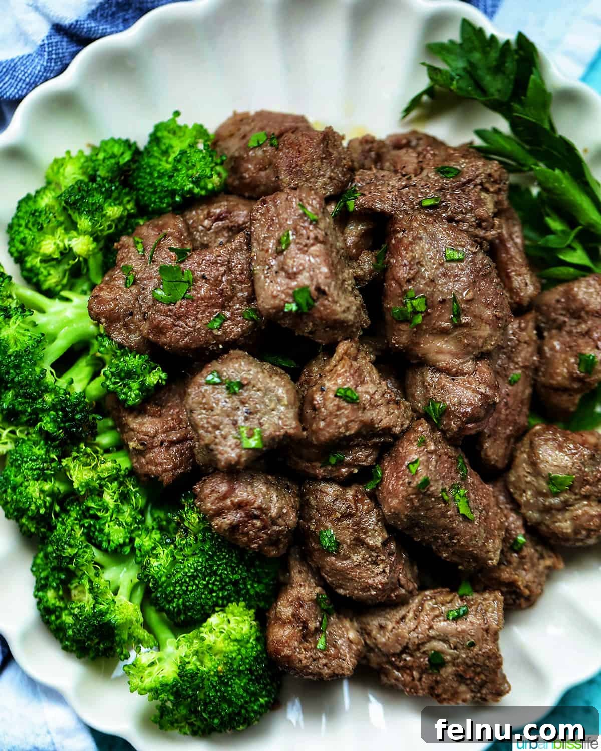 Effortless Air Fryer Steak Morsels 13 air fryer steak bites with chopped parsley garnish and a side of broccoli on a plate.
