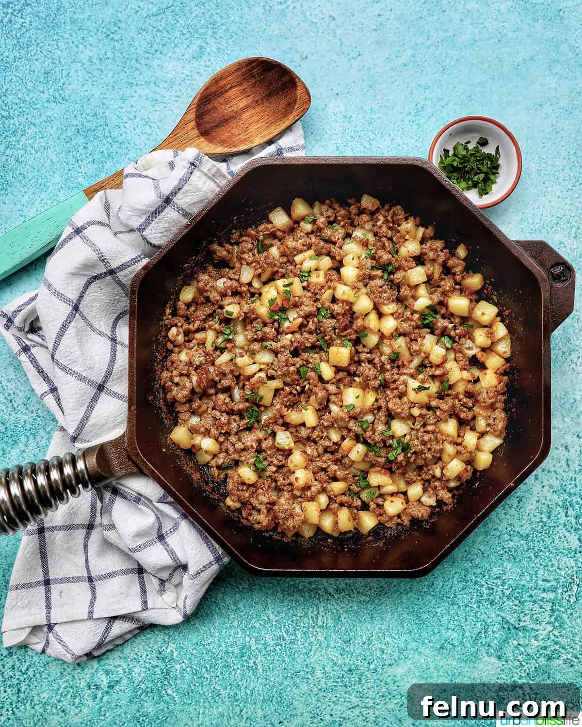 Sizzling Sausage Potato Hash 21 Overhead view of breakfast sausage potato hash in a cast iron skillet with a wooden spoon.