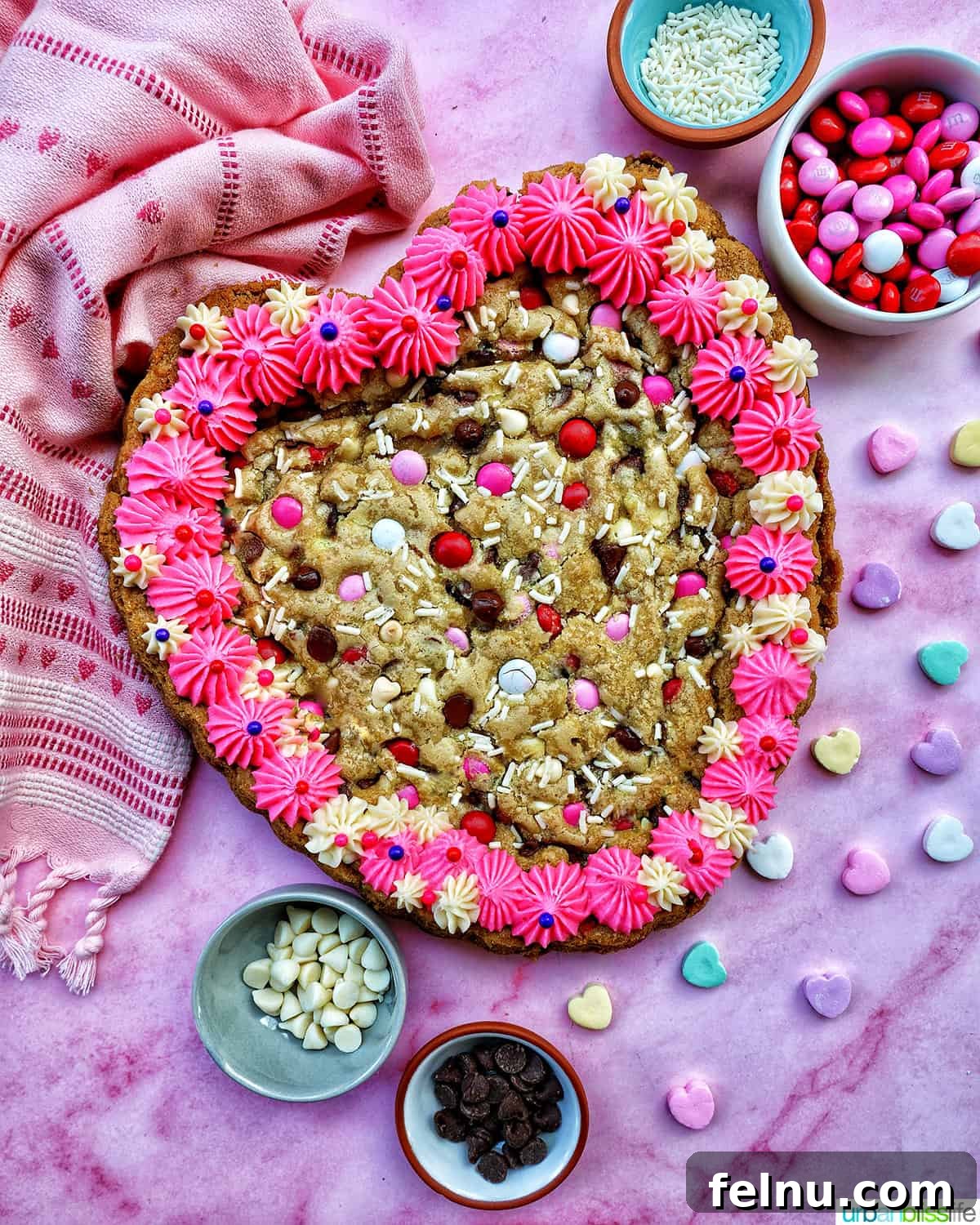 Love Struck Cookie Cake 2 A Valentine's Day Cookie Cake with pink frosting, pink, red and white M & M candies, conversation hearts candies sprinkled around the cookie cake, and white sprinkles.