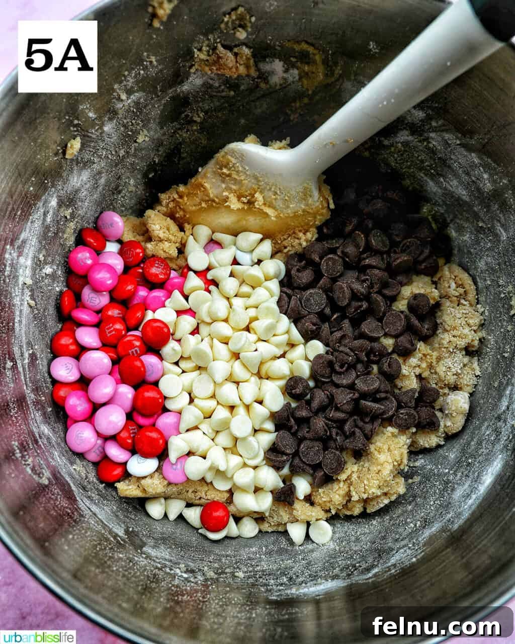 Love Struck Cookie Cake 11 M & Ms, white chocolate chips, and semi-sweet chocolate chips added to batter in a stand mixer bowl.