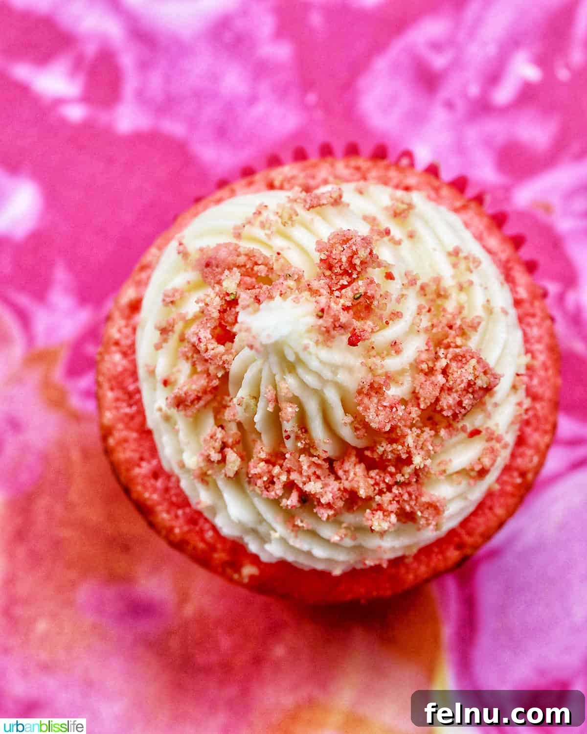 Strawberry Shortcake Crunch Cupcakes 25 A vibrant strawberry crunch cupcake presented overhead against a bright pink swirled background, emphasizing its appealing topping.